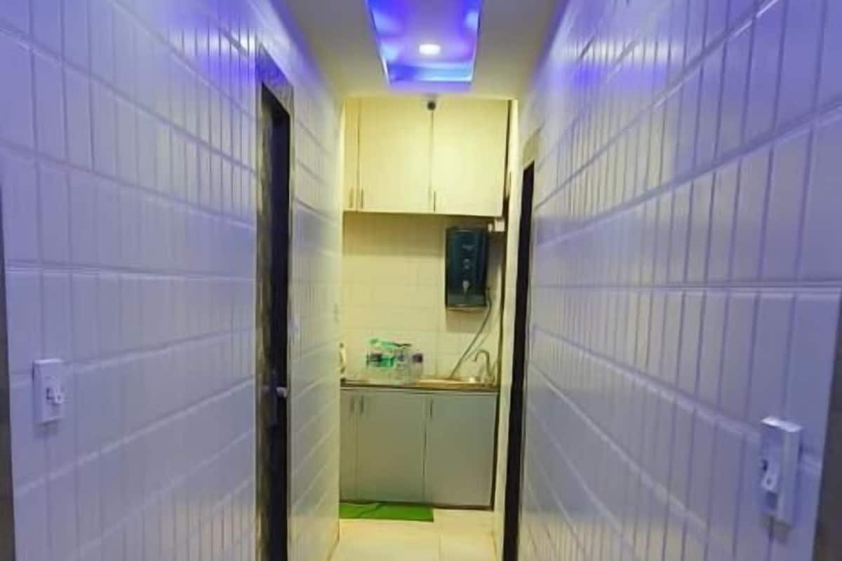 A narrow hallway with white tiled walls and a tiled floor leading to a kitchen area with cabinets and a countertop.