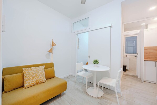 A modern living room with a mustard sofa, a small round table, and a white chair. - La Latina Jewel Seasonal Rental (Madrid)