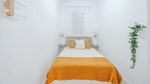 Habitación de hotel estrecha con una cama, un ventilador de techo, un espejo y una planta colgada en la pared.