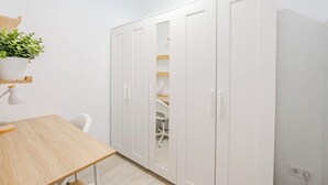 Una habitación con una mesa de madera, un armario blanco y una planta en una estantería.