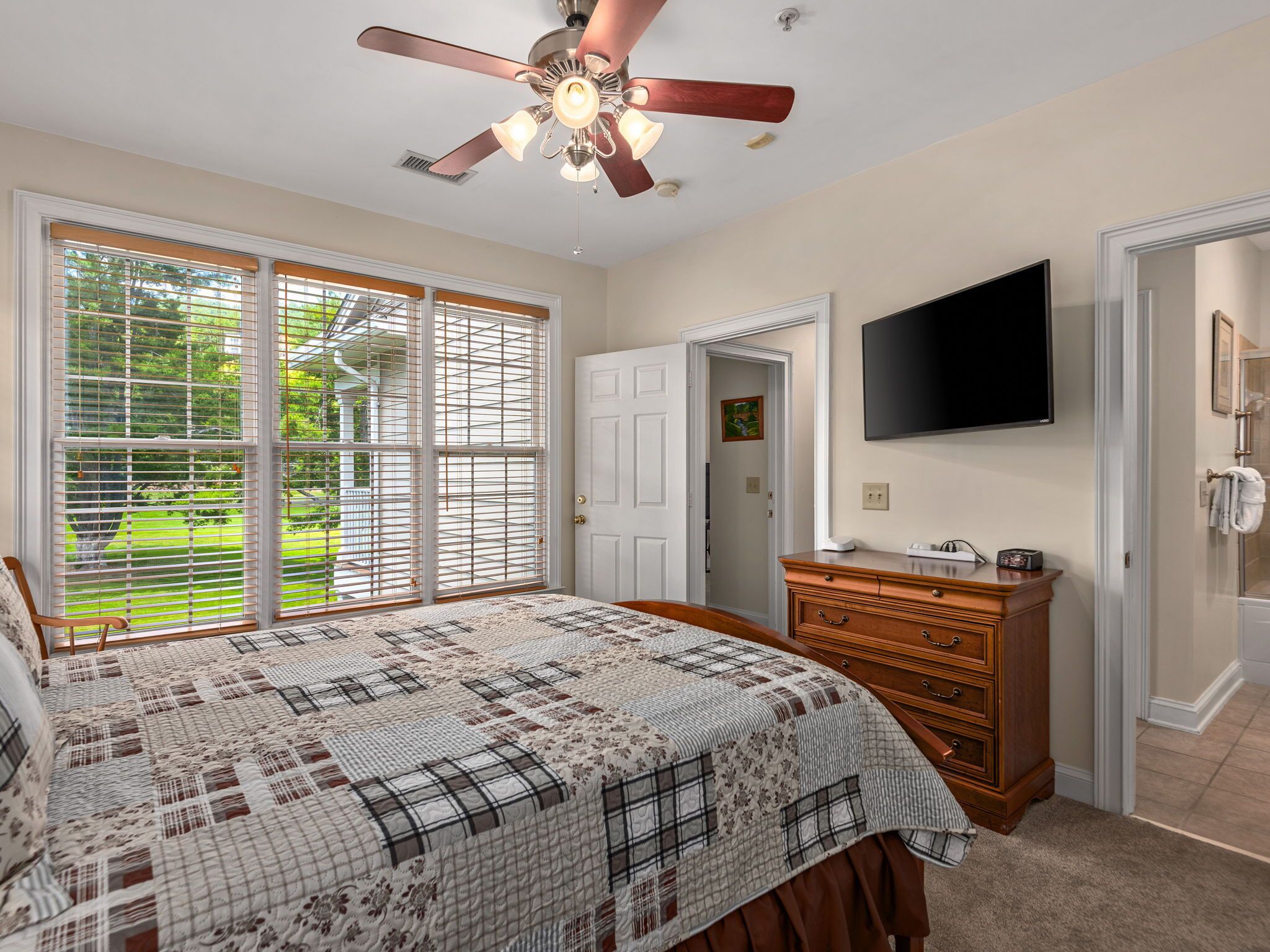 A bedroom with a large bed, a ceiling fan, a TV, and a dresser.