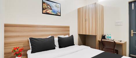 A hotel room with a bed, a desk, a chair, and a painting on the wall.