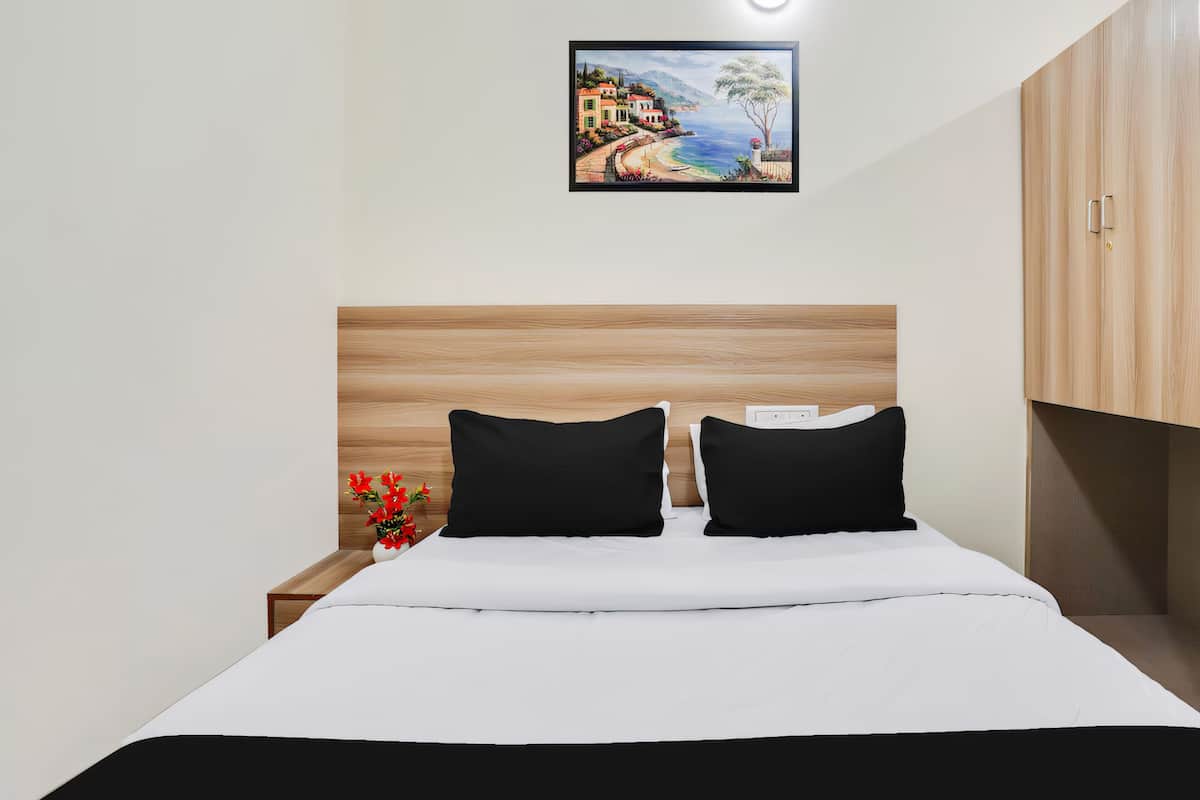 A neatly made bed with black pillows, a white comforter, and a small vase with red flowers on a wooden nightstand.