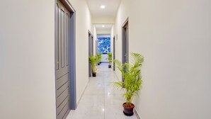 A clean, narrow hallway with white walls and a tiled floor, leading to a bright room with a large window. - RG Suites HSR (Bengaluru)