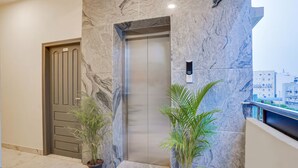 A modern elevator with a marble wall, a door with a number plate, and potted plants. - RG Suites HSR (Bengaluru)