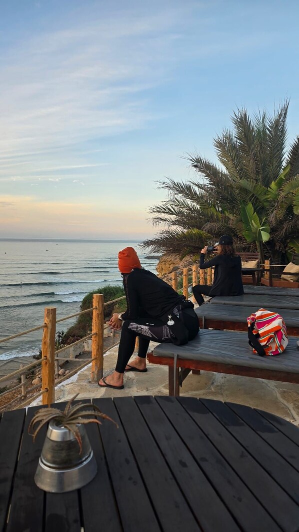A wooden deck overlooking the ocean with a person sitting on a bench. - Aloha imsouane chambres (Imsouane)