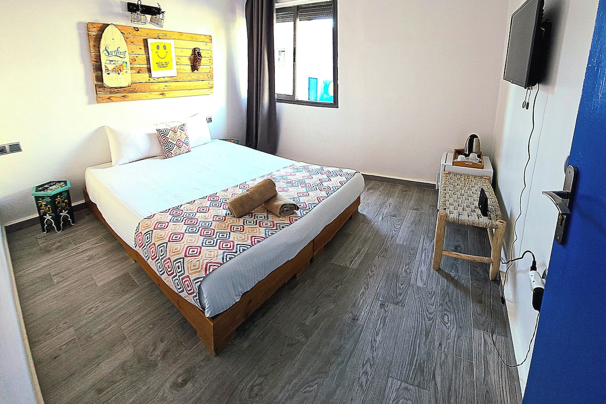 Un dormitorio con cama, televisor, ventana y una obra de arte colgada en la pared.