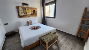 A bedroom with a bed, a wooden bench, a surfboard decoration, and a window with curtains. - Aloha imsouane chambres (Imsouane)