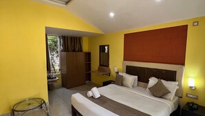 A hotel room with a bed, a nightstand, a desk, a chair, a ceiling fan, and a window with curtains.