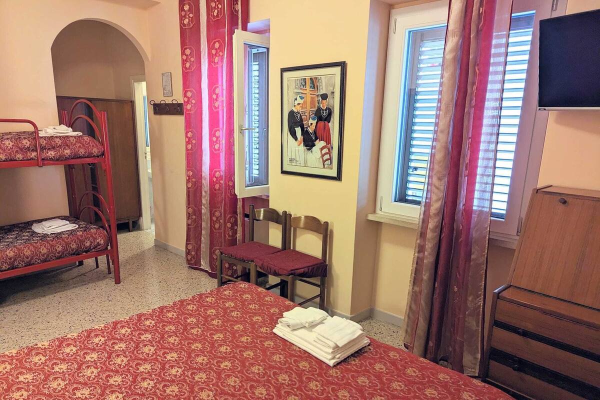 Une chambre avec un lit superposé, un lit simple, une chaise, un bureau, une fenêtre et un tableau encadré au mur.