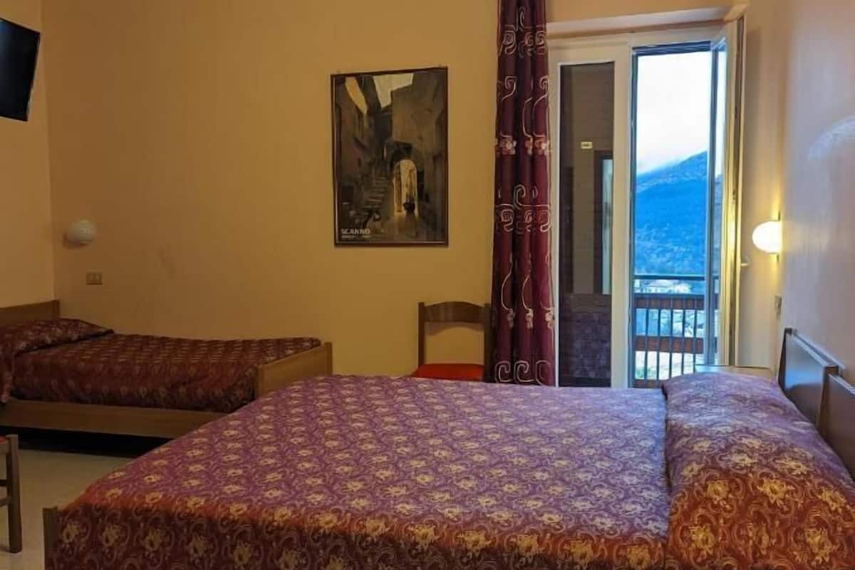 Une chambre d’hôtel avec deux lits simples, un bureau avec une chaise, un tableau au mur et un balcon avec vue.