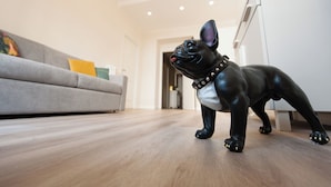 A black dog figurine on a wooden floor in a modern living room with a grey sofa and a white cabinet. - Design 18 Charming Rooms (Rome)