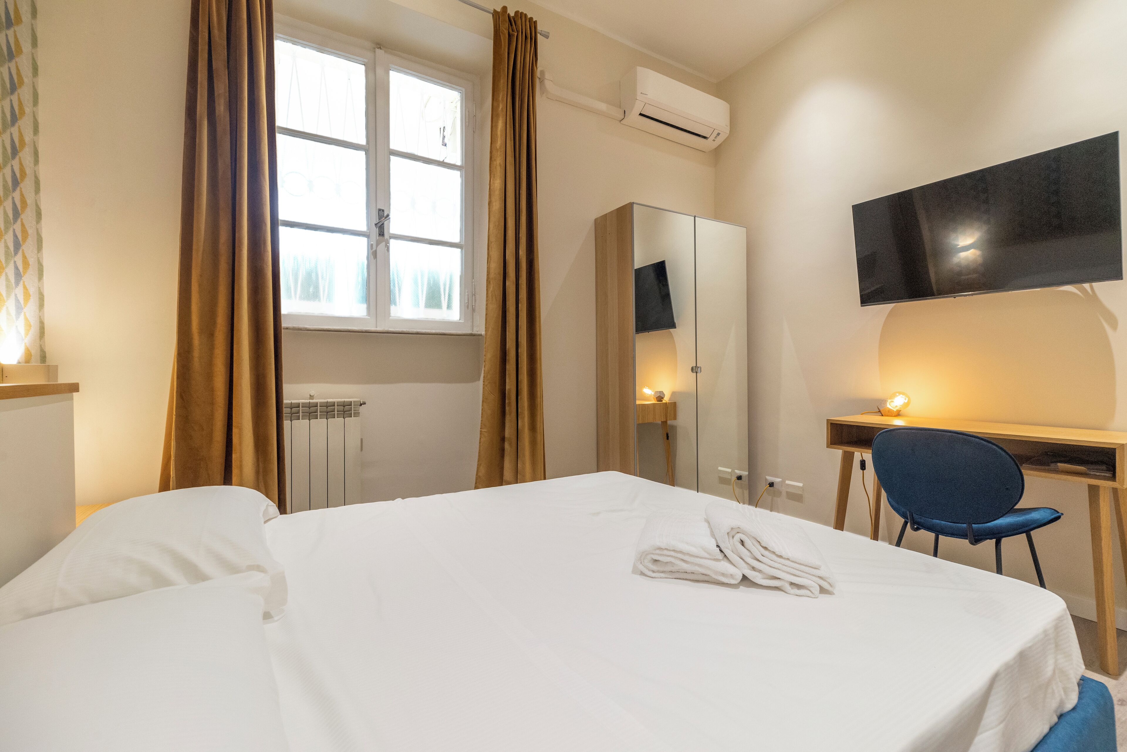 Habitación de hotel con cama, escritorio, silla, televisor y ventana con cortinas.