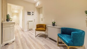 A modern living room with a light wood floor, a blue sofa, a mustard-colored armchair, and a white cabinet with a plant. - Design 18 Charming Rooms (Rome)