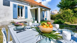 A dining table set outdoors with a bowl of fruit, plates, and cutlery.