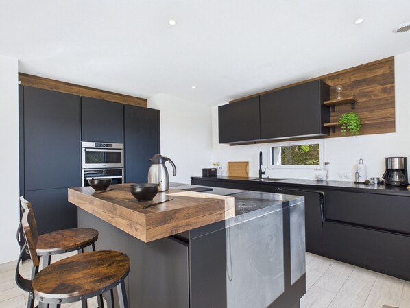 Una cocina moderna con armarios oscuros, una isla de madera, electrodomésticos de acero inoxidable y un ventanal que proporciona luz natural.