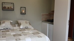 A bedroom with a large bed, a small bedside table, a wall-mounted shelf with decorative items, and a door leading to the bathroom. - La Chambrée (Leschelle)