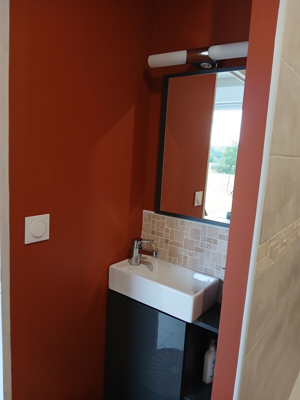 A bathroom with a white sink, a mirror, and a red wall. - La Chambrée (Leschelle)