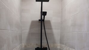 A shower area with a handheld showerhead, a handheld scrubber, and a red bucket. - La Chambrée (Leschelle)