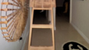 Een houten trap die uitkomt op een plateau, met een ventilator aan de muur en een lijst met een afbeelding.