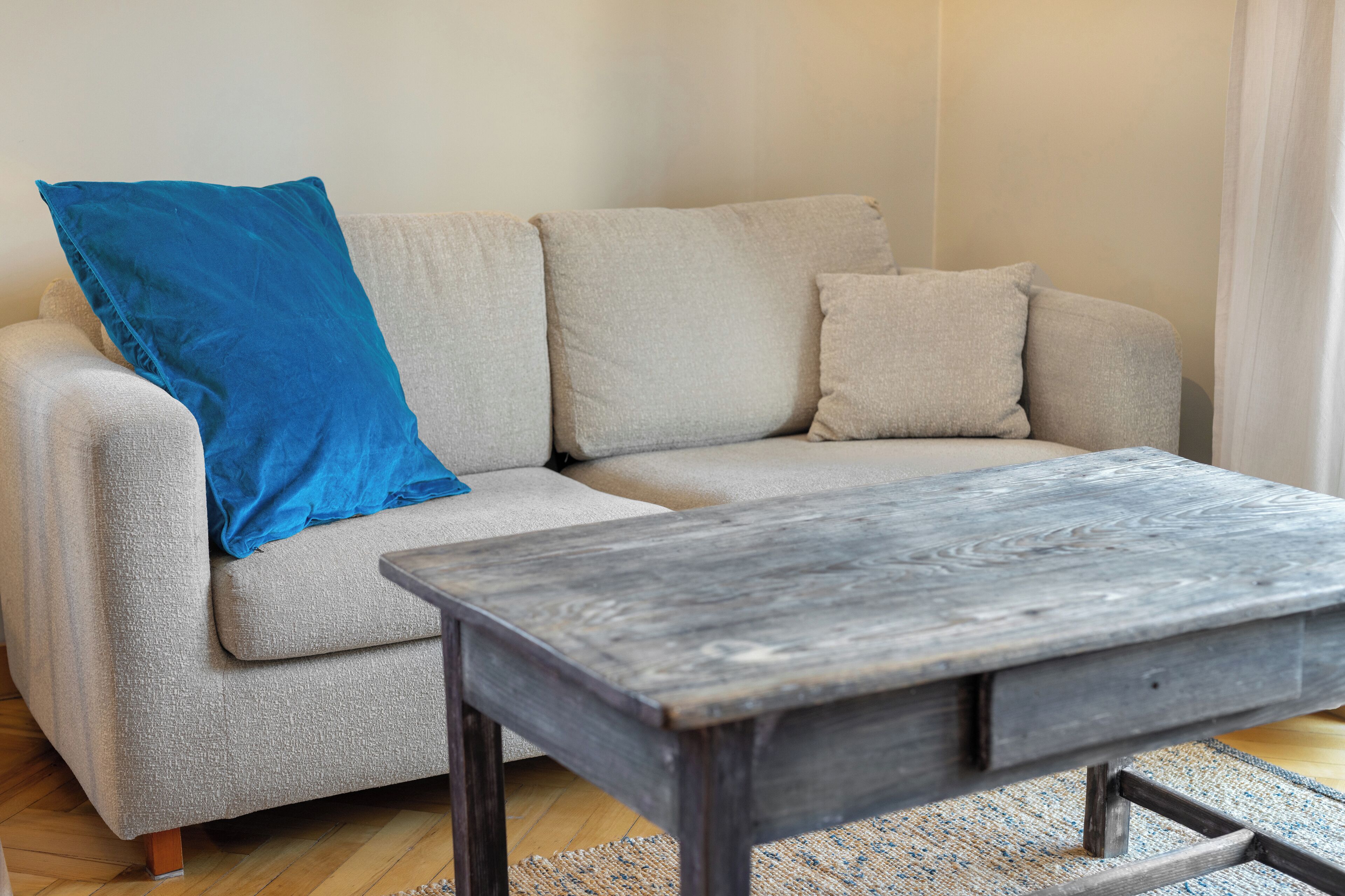 Una sala de estar con un sofá gris, un cojín azul y una mesa de centro de madera.