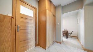Un pasillo con puertas de madera, un comedor con mesa y sillas, y suelo de baldosas.