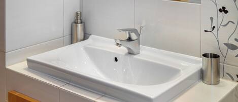 A modern bathroom with a white sink, a silver faucet, and a stainless steel cup on the counter.