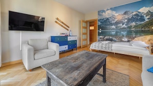 Una sala de estar moderna con un televisor de pantalla plana, un sofá, una mesa de centro y un cuadro de un paisaje montañoso.