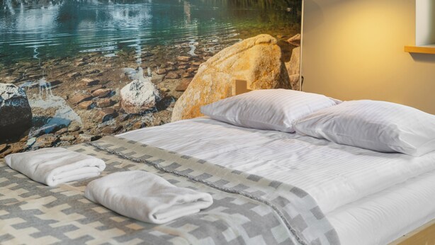 Un dormitorio con cama, almohadas y una colcha. Hay una roca grande y una lámpara en la pared.