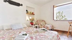Un dormitorio con una cama grande, una silla, una mesita y una ventana con vistas a árboles.