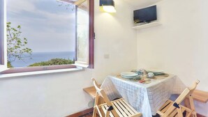 Habitación de esquina con una mesa lista para dos personas, un televisor montado en la pared y ventana con vistas al mar.