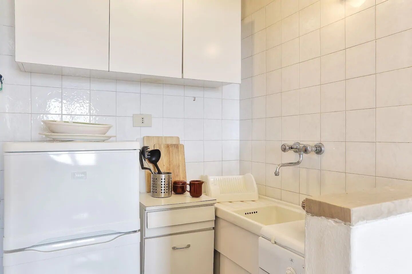 A compact kitchen with white cabinets, a white refrigerator, a sink, and a wooden cutting board.