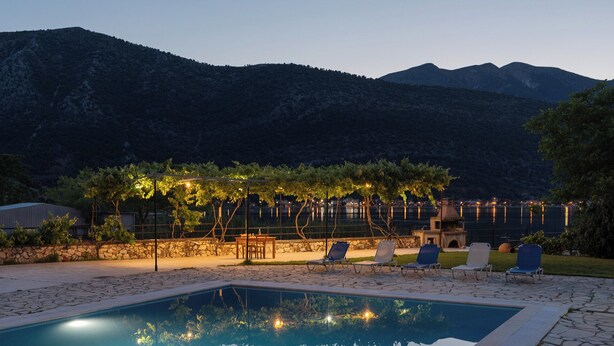 Un espace piscine avec des chaises longues, une pergola illuminée et un mur en pierre.