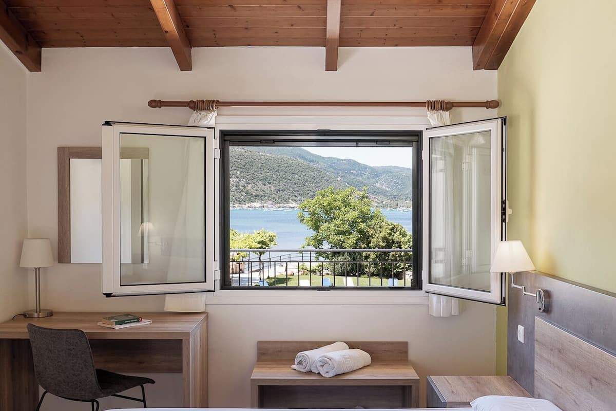 Un dormitorio con cama, escritorio y ventana con vista a un lago y árboles.