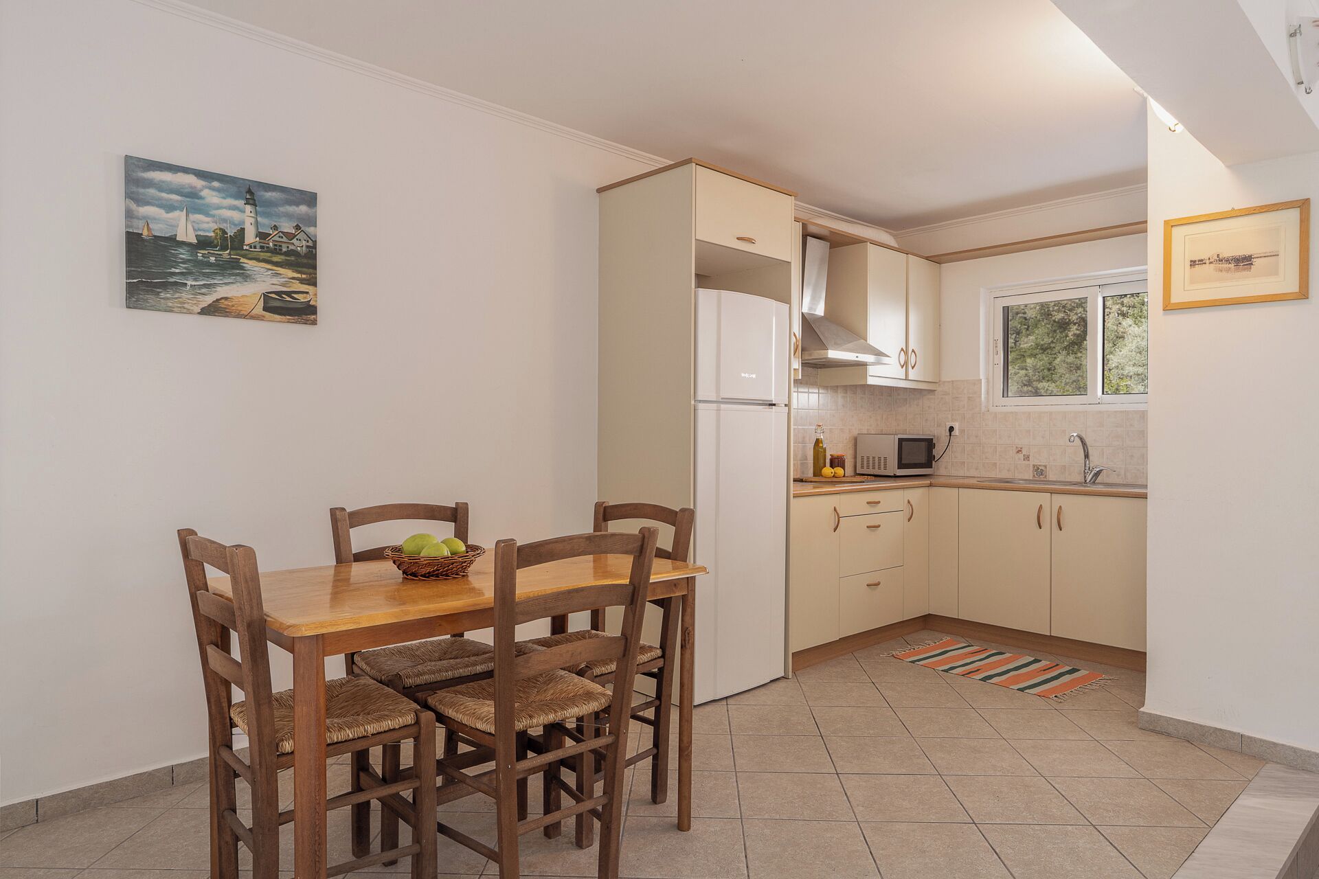 A compact kitchen with a dining table and chairs, a refrigerator, a microwave, and a window with a view of greenery.