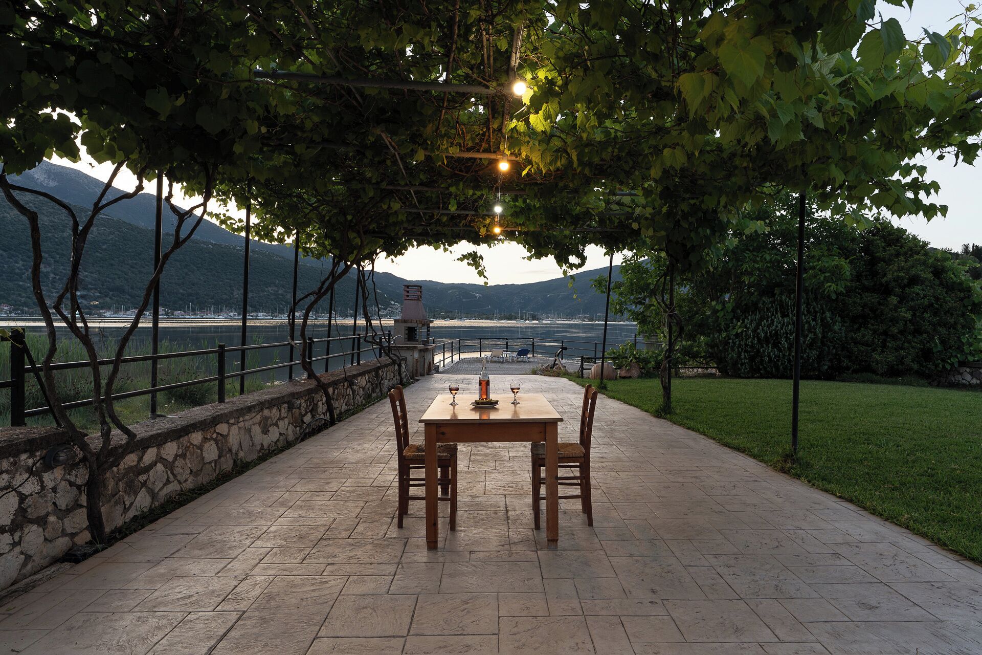 An outdoor dining area with a table and chairs, overlooking a body of water and mountains.