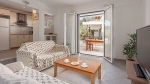 Un salon moderne avec un canapé, une table basse et un téléviseur. Un balcon donne sur un coin repas et une cuisine, qui sont visibles à travers les portes vitrées.