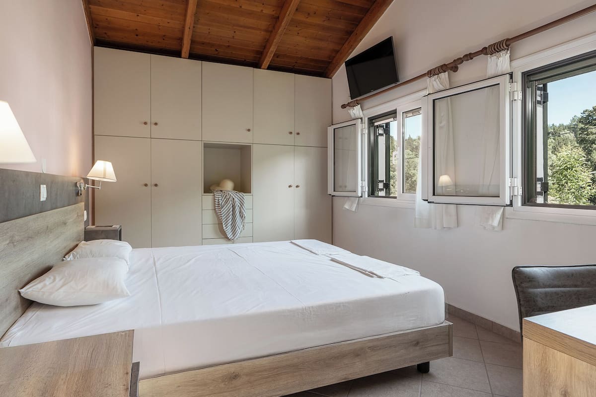 Un dormitorio con cama, mesita de noche, armario y ventana con cortinas.