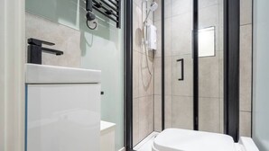 A modern bathroom with a glass shower enclosure, a toilet, and a towel rack. - Cosy Nook | Kitchen w/ Washer & SofaBed | Free Parking (Merseyside)