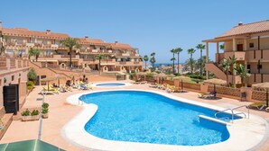 A resort with a large swimming pool, multiple balconies, and palm trees.
