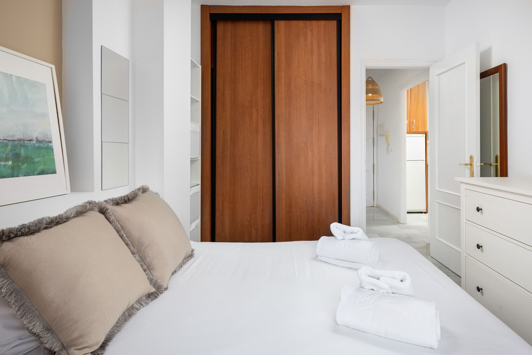 Une chambre d’hôtel avec un lit, une armoire en bois, une commode blanche et un tableau encadré au mur.
