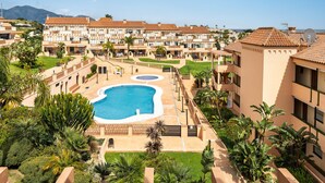 A resort with multiple buildings, a central swimming pool, and surrounding greenery.