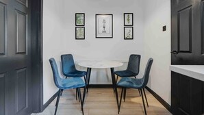 A dining area with a round table and four blue chairs, a white ceiling light, and framed artwork on the wall. - 10Min Walk to Stadium | SofaBed | W/M & Dishwasher (Anfield)