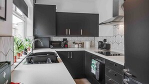A modern kitchen with black cabinets, a white countertop, and a built-in oven. - 10Min Walk to Stadium | SofaBed | W/M & Dishwasher (Anfield)
