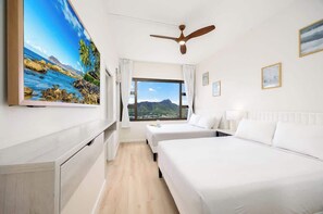 Ein Hotelzimmer mit zwei Betten, einem Deckenventilator, einem großen Fenster mit Bergblick und einem Bild an der Wand.