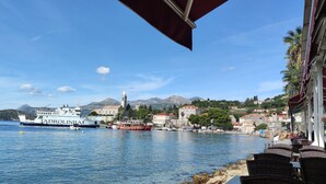 A coastal town with boats docked, a prominent white ship with 'JADROLINIA' written on it, and a view of the town's buildings and mountains in the background.