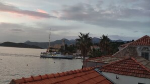 A coastal town with a calm harbor, a prominent church with a tall steeple, and a mountain range in the background.