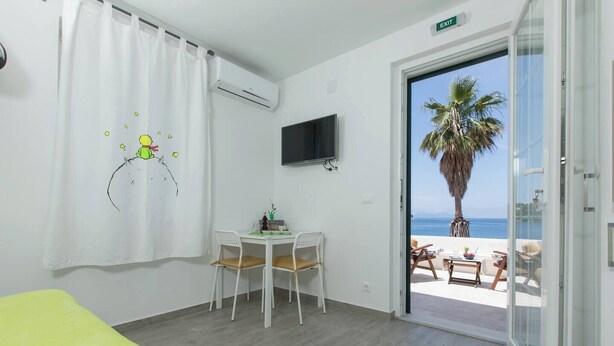 A room with a bed, a table with chairs, a TV, and a view of the beach.