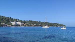 A coastal scene with a sailboat on the water, buildings on a hillside, and a clear sky.