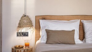 A bedroom with a wooden headboard, white bedding, a woven lamp, and a small wooden side table with a glass of orange juice. - Nomada 1 | Chania City Center (Chania)